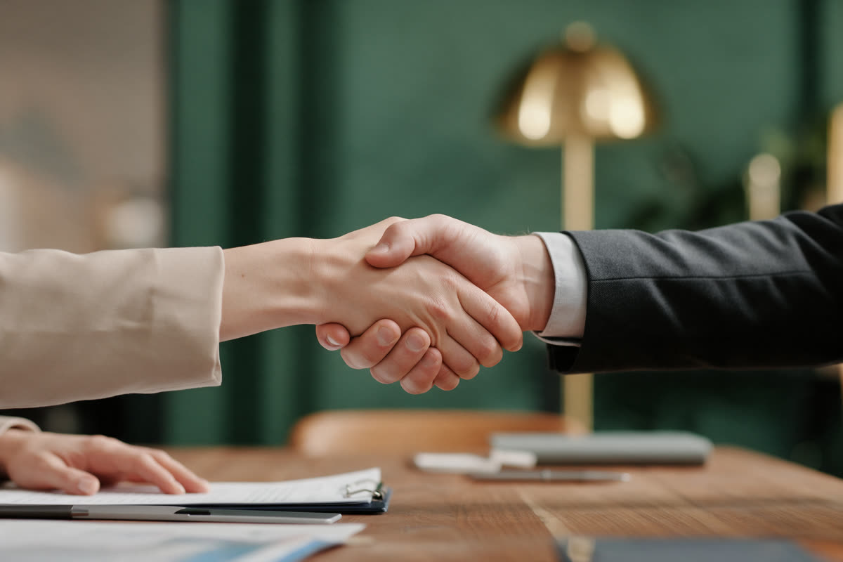 Two people shaking hands across a wooden conference table